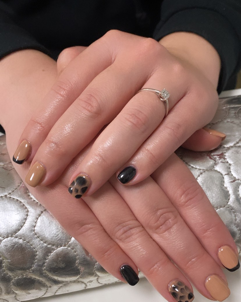 Korte nagels in nude, zwart en luipaardprint op een zilveren tas